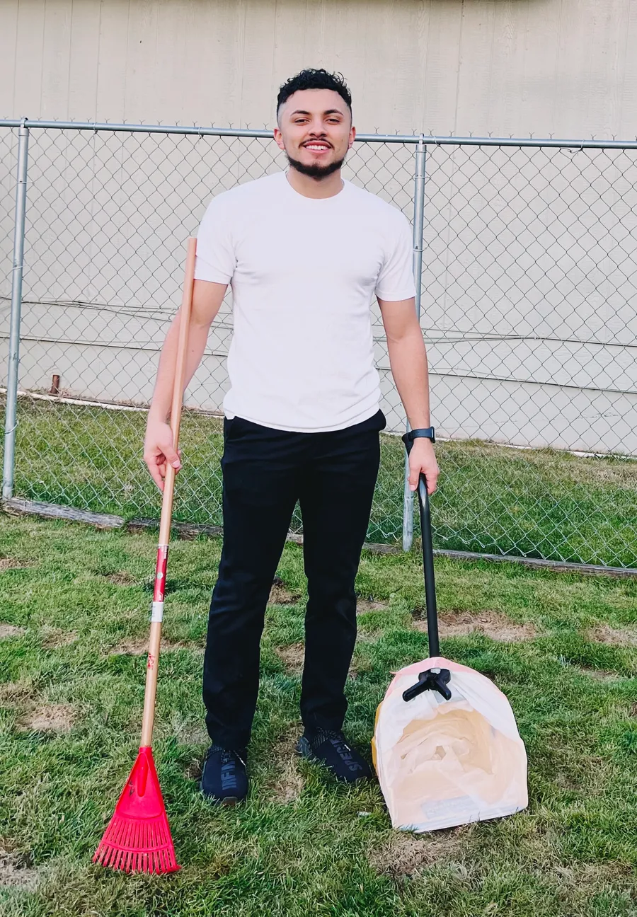 Saul, owner of Scoopable, in a clean backyard with his rake and scooper